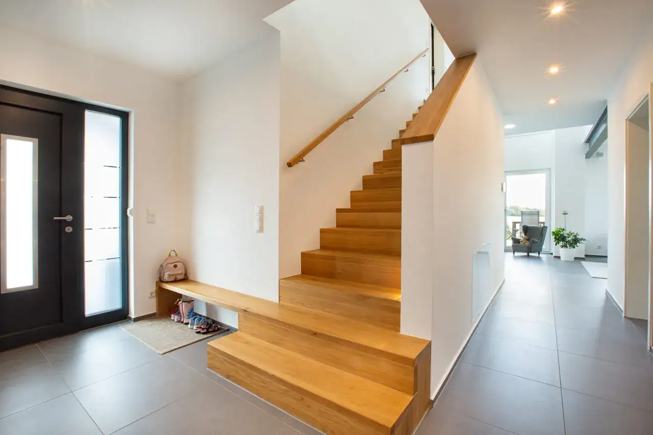 Moderne Ideen für den Hauseingang: Eine Holztreppe mit integrierter Sitzbank und Schuhablage lädt zum Eintreten ein.