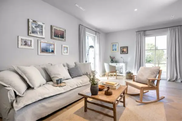 Gemütliches Wohnzimmer in millennial grey mit großem Sofa, Holztisch und Schaukelstuhl. Bilderrahmen zieren die Wand.