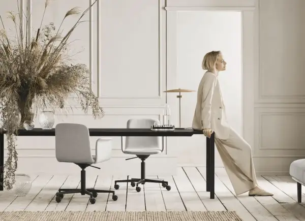 Moderne Büroumgebung mit hellen Wandfarben, einem großen Tisch, zwei Stühlen und einer Frau im Anzug.