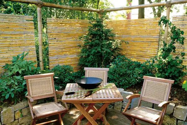 Ausgefallener Sichtschutz Garten selber machen: Bambusmatten und Holzmöbel schaffen eine gemütliche Ecke.