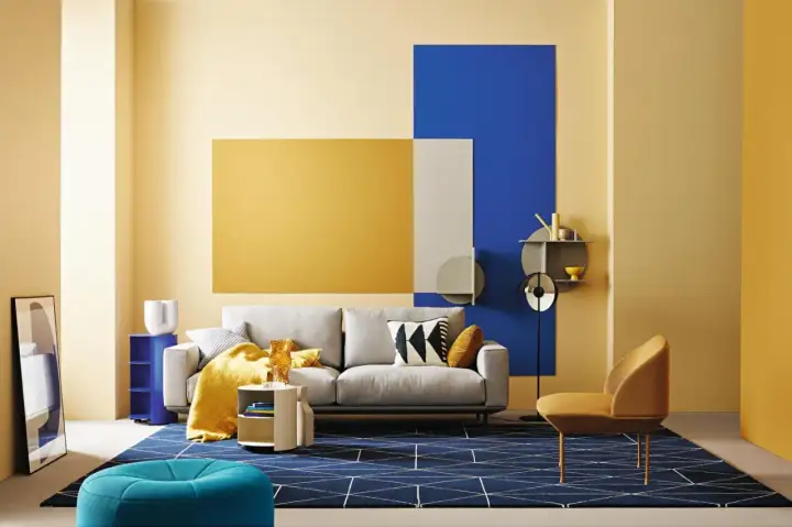 Modernes Wohnzimmer mit gelber Wandkunst, die die Farbe Gelb und ihre Bedeutung von Freude und Optimismus hervorhebt. Ein graues Sofa, ein blauer Teppich und ein gelber Sessel.